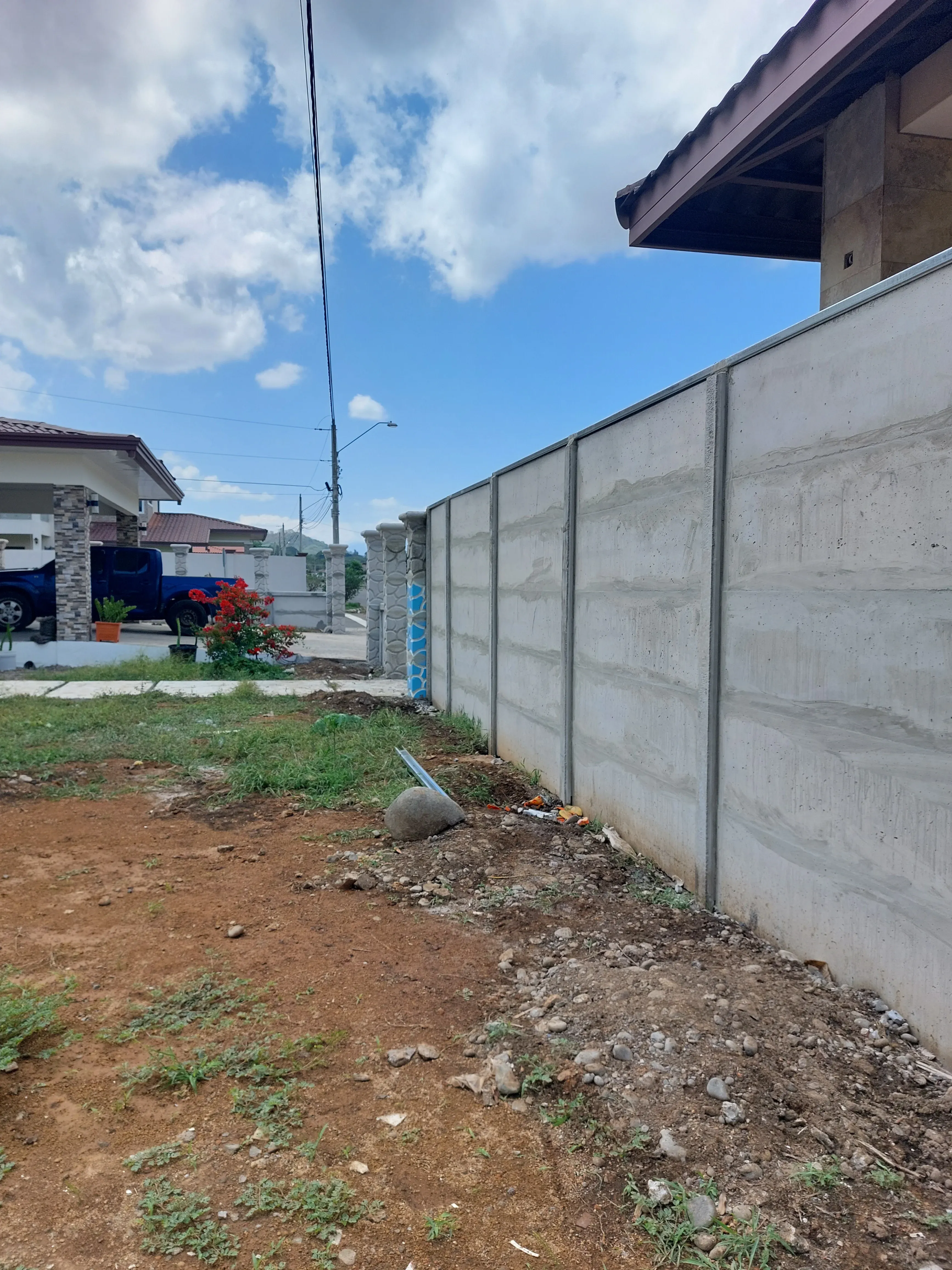 Muro perimetral prefabricado visto desde el interior de un lote vacío con residencia al fondo