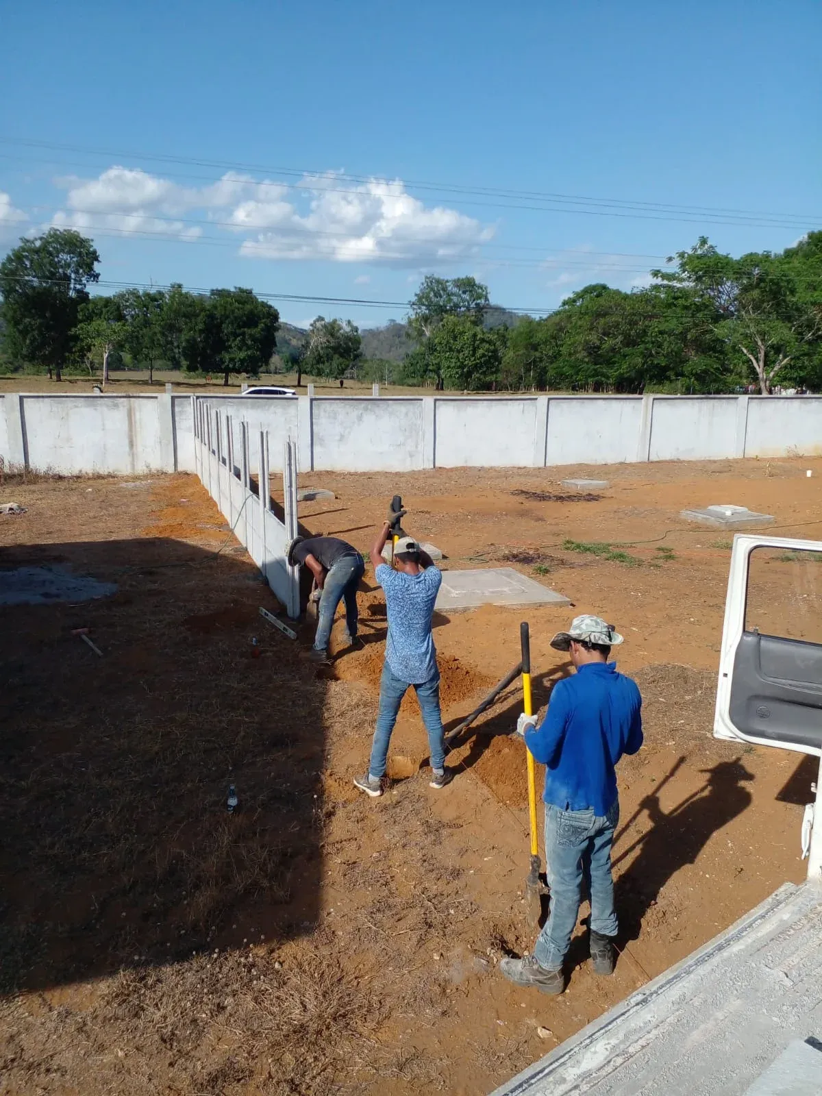 Cuadrilla instalando muro perimetral prefabricado en lote rural amplio con horizonte despejado