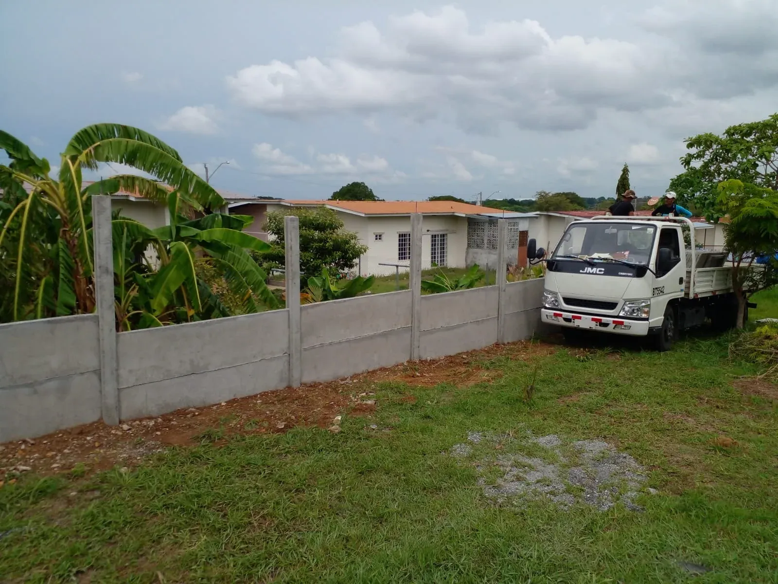 Muro perimetral prefabricado en lote residencial con camión y vegetación tropical al fondo