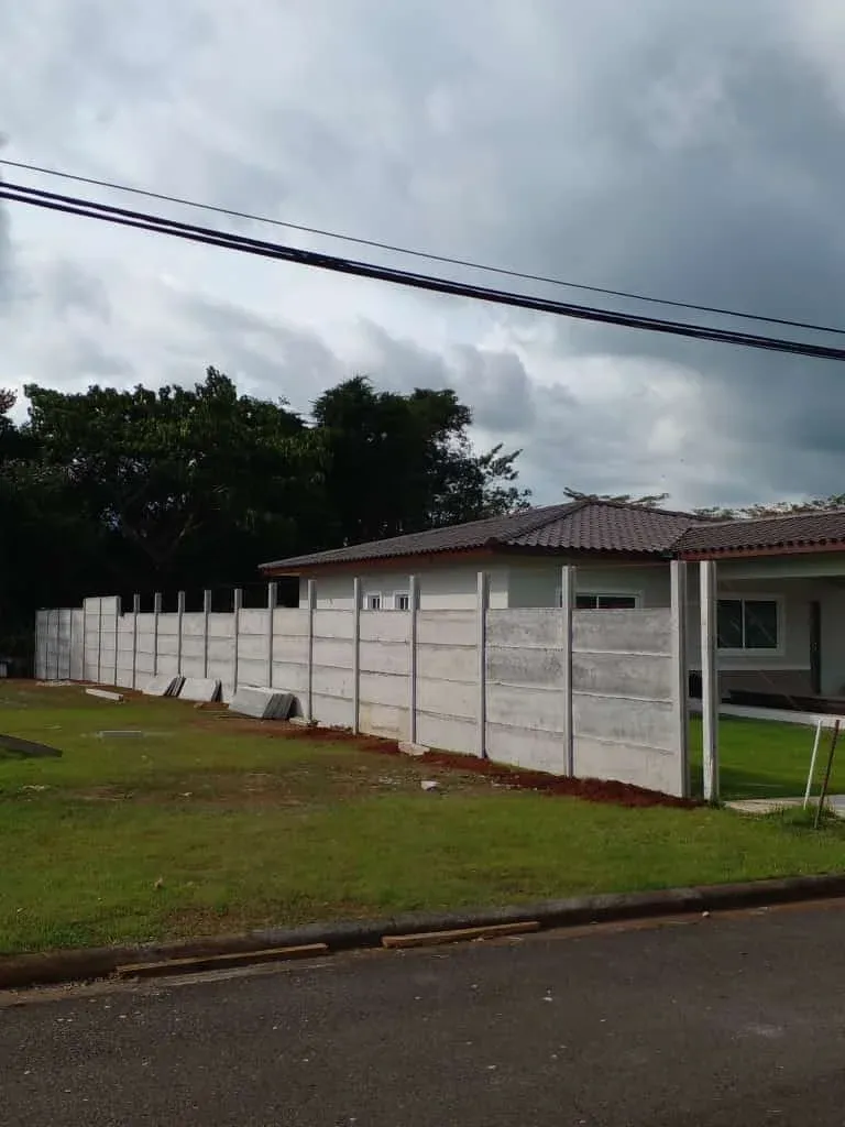 Muro perimetral prefabricado largo con perspectiva en frente de vivienda y calle pavimentada