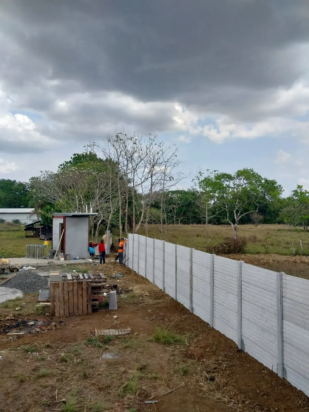 Muro perimetral prefabricado largo en lote rural con cielo nublado y horizonte abierto
