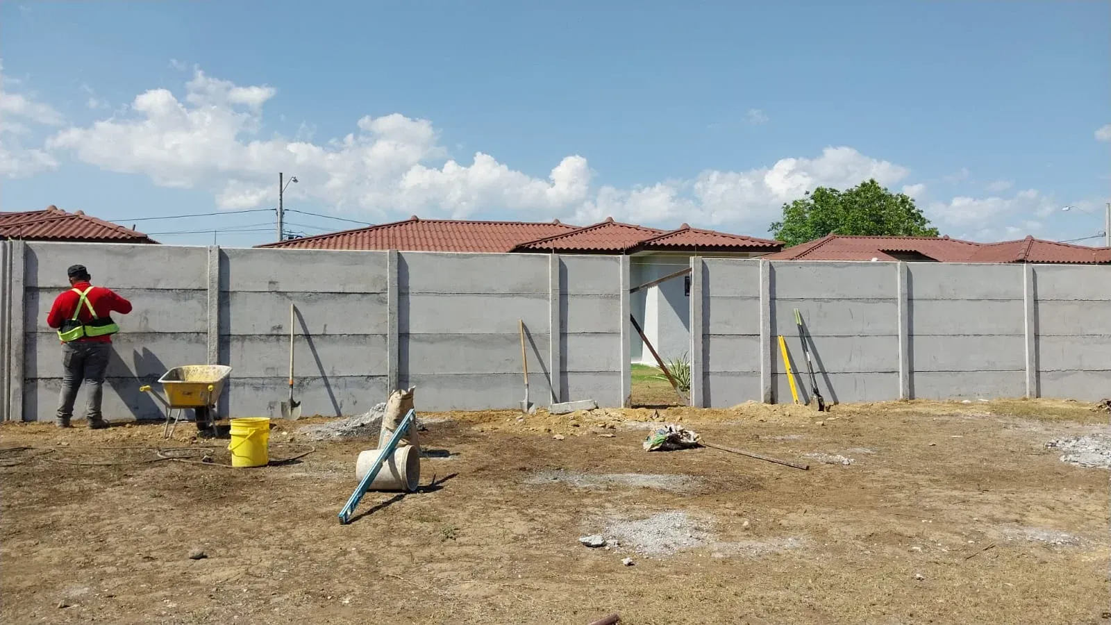 Lote con muro perimetral en construcción y operario al fondo junto a viviendas terminadas
