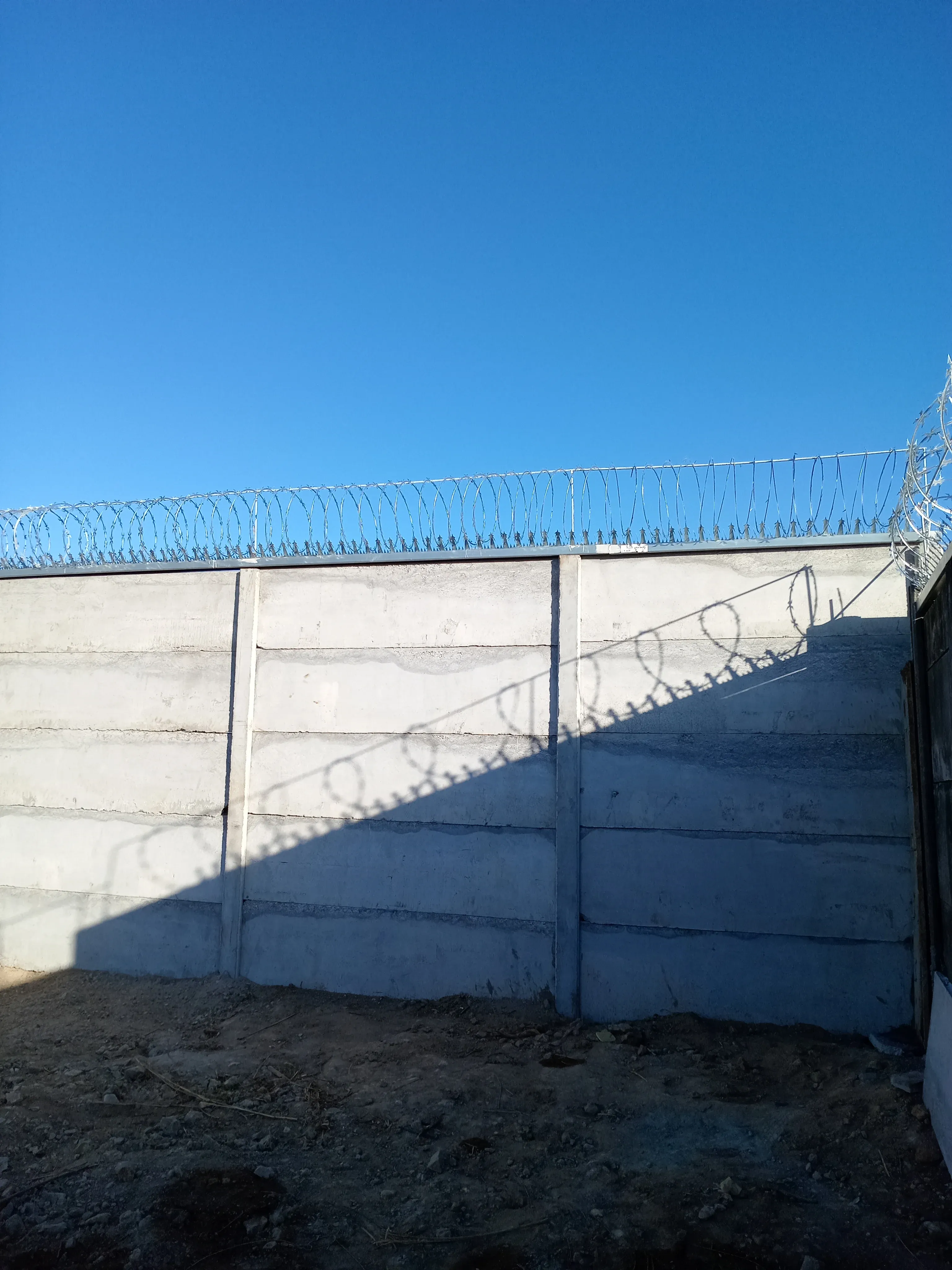 Muro perimetral prefabricado alto con alambre de púas superior bajo cielo despejado