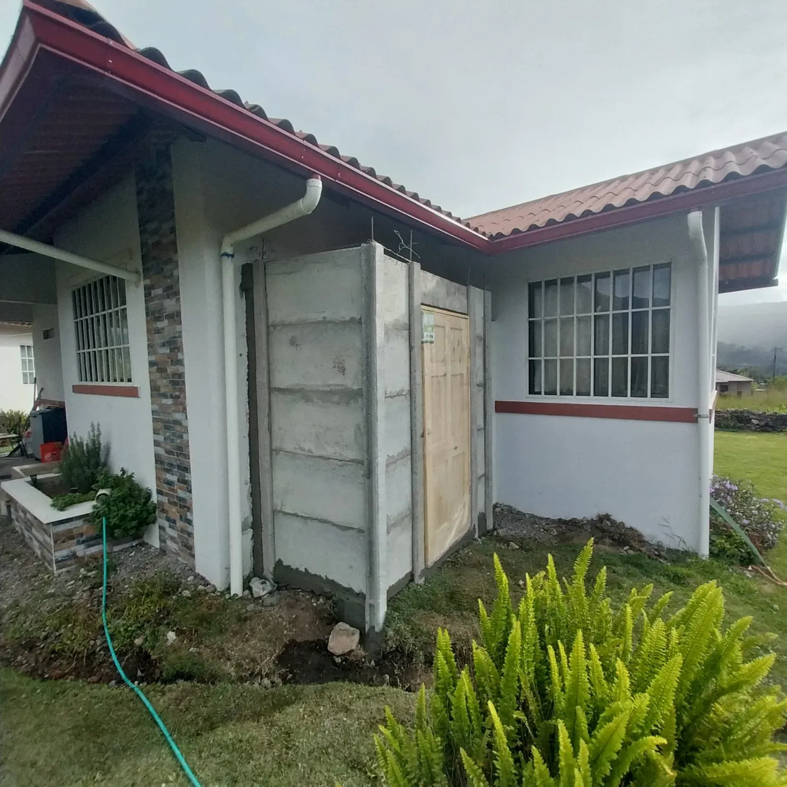 Anexo de muros de concreto recién instalado entre dos viviendas en jardín residencial